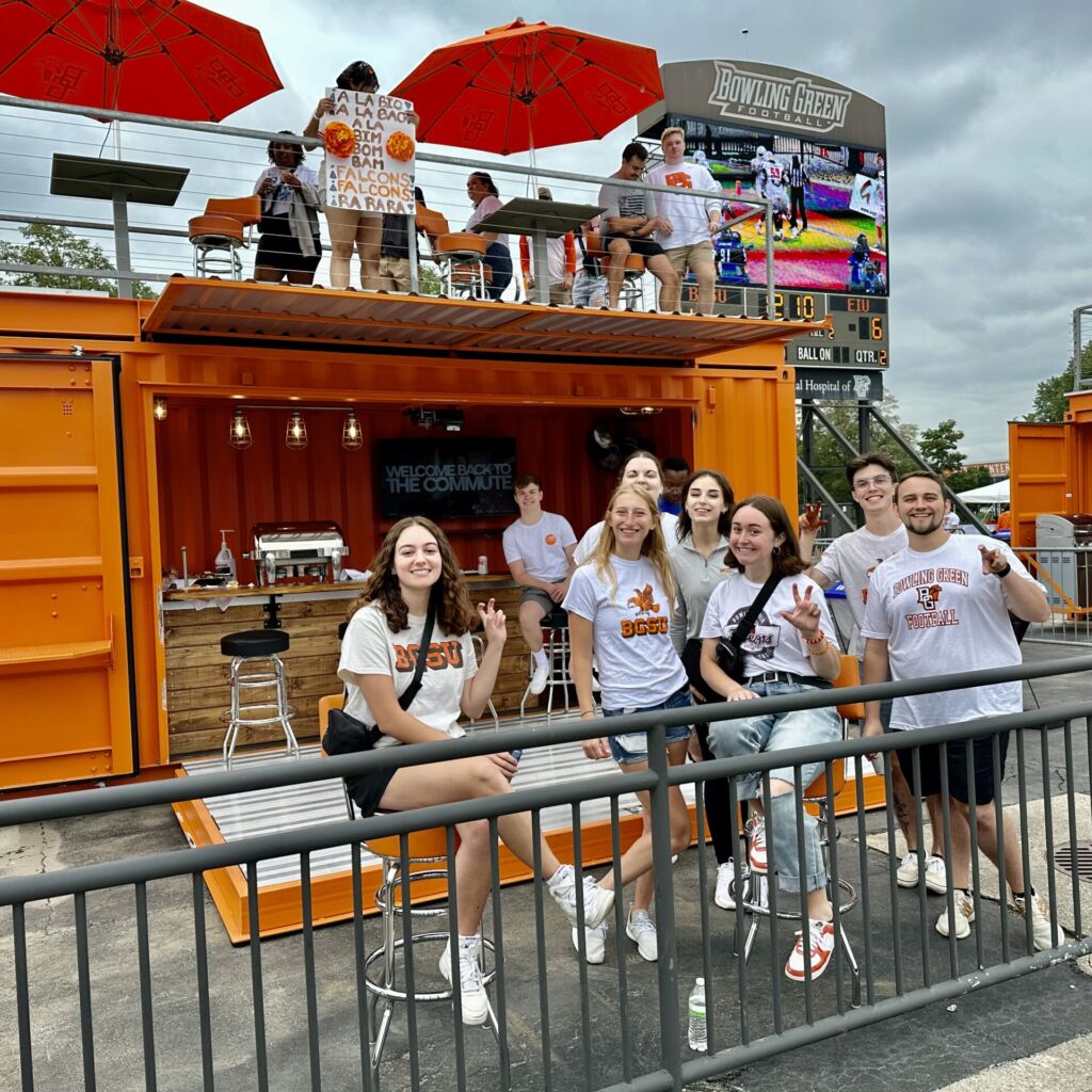 A group of people standing around in front of an orange container.