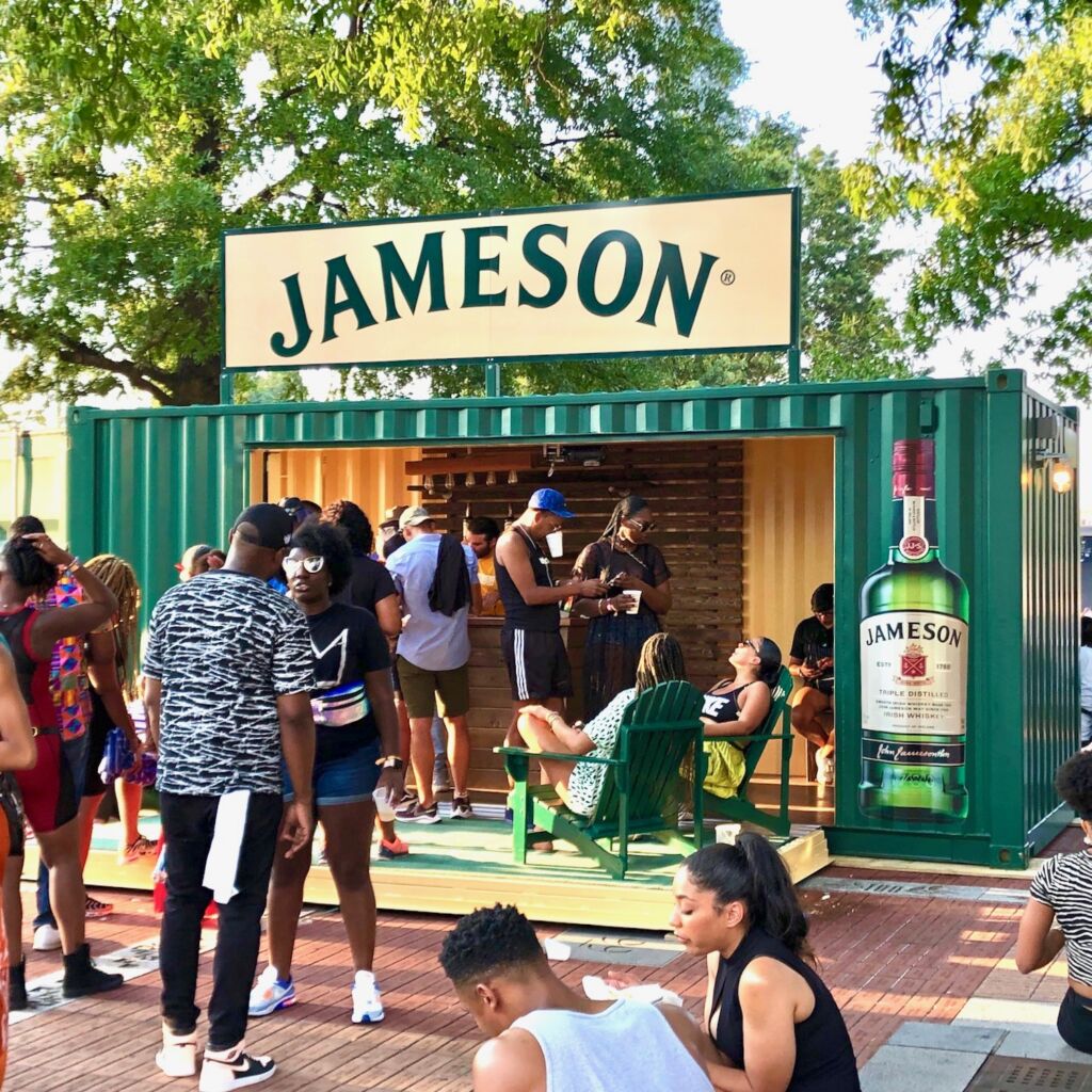 A group of people standing around outside in front of jameson.