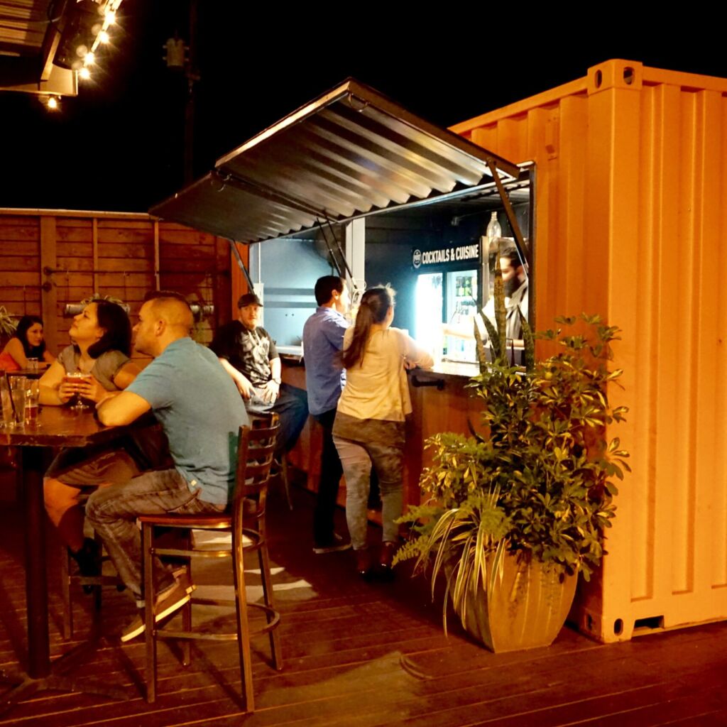 A group of people are sitting at tables in front of an outdoor bar.